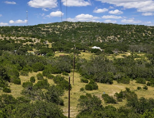 3E Ranch power line crossing brushy pasture toward buildings below a wooded hill
