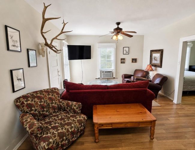 3E Ranch living room with red sofa, leather recliners, ceiling fan, and TV
