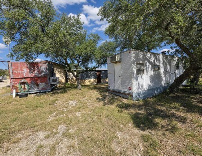 3E Ranch white portable building and red shed shaded by oak trees