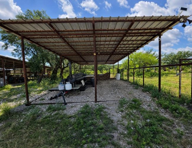 3E Ranch metal carport sheltering smoker trailer, propane tanks, and firewood