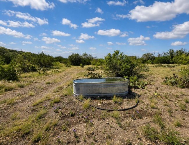 3E Ranch galvanized water trough beside a dirt trail and prickly pear