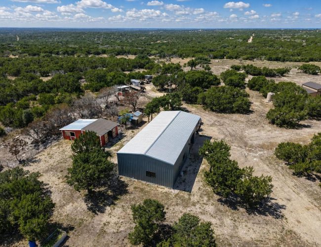 C&P Ranch aerial of the gray metal barndominium and red outbuildings, Edwards County, Texas